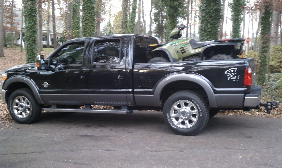 Black crew cab pickup truck with an ATV in the bed, parked on a driveway