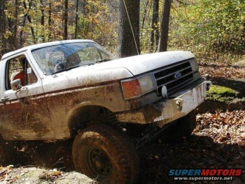 1989 Ford Bronco - A white Ford Bronco navigates a muddy trail through the woods during autumn.