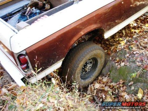 1989 Ford Bronco - A brown and white Ford Bronco is stuck in the mud, with its rear tire partially submerged.