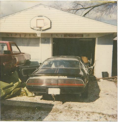 1978 Pontiac Trans Am - A black 1978 Pontiac Trans Am is parked in a garage, partially obscured by a red pickup truck and green tarp.