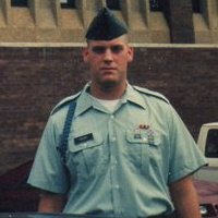 1989 Ford Bronco - A man in a military uniform stands in front of a building with a vehicle partially visible behind him.