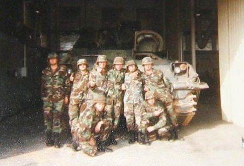 1989 Ford Bronco - A group of soldiers poses with a military vehicle in what appears to be a garage or hangar.