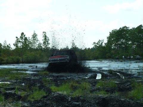 1995 Ford Bronco - A red SUV navigates a muddy track, creating a large spray of mud and water.