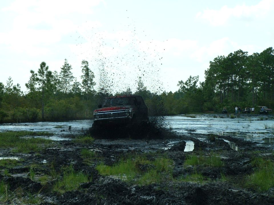 Red SUV splashing through mud, throwing water and dirt high into the air