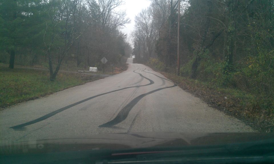 Winding rural road with dark tire marks, trees and grass on the sides