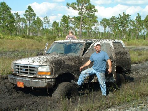 1995 Ford Bronco - A mud-caked Ford Bronco is stuck in a swampy area with two men nearby.