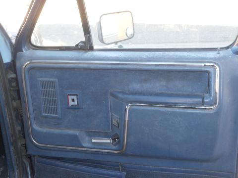 1986 Ford Bronco - Close-up of a vehicle's blue interior door panel, showing the speaker grille and door handle.