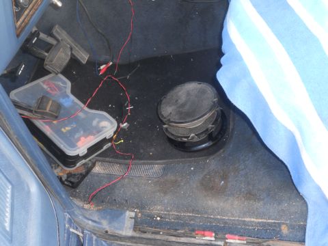1986 Ford Bronco - The interior floor of a vehicle shows a speaker, a toolbox filled with wiring, and pedals.