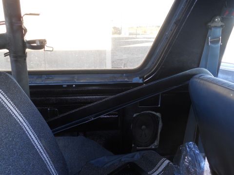 1986 Ford Bronco - The interior of the vehicle features a roll cage and a visible speaker mounted on the side panel.