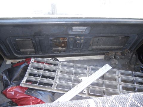 1986 Ford Bronco - A silver grille and various engine parts are stored in the cargo area of a vehicle.