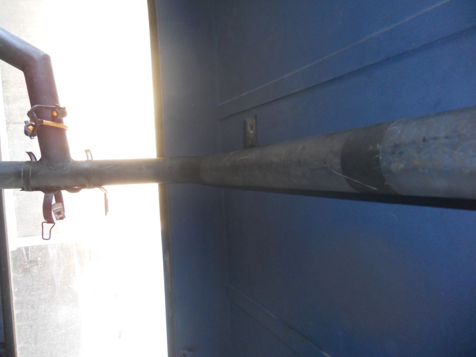 Close-up of a pipe running along the blue interior wall of a vehicle, with a strap and clamp visible