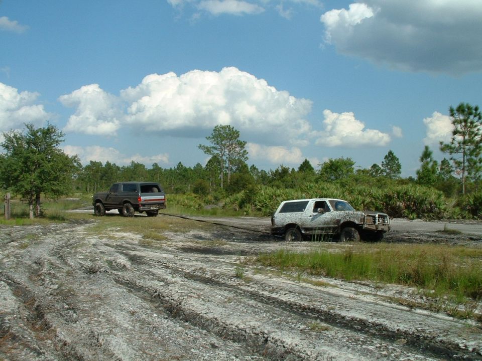 dark SUV pulling white SUV out of mud pit