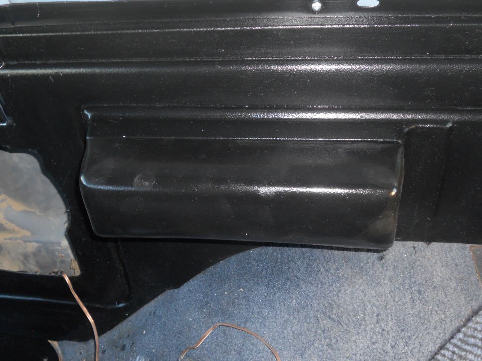 Black dashboard compartment with textured surface and a pull handle. Blue carpet visible below