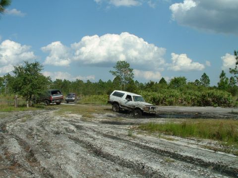 1995 Ford Bronco - Multiple SUVs navigate a muddy off-road course under a cloudy sky.
