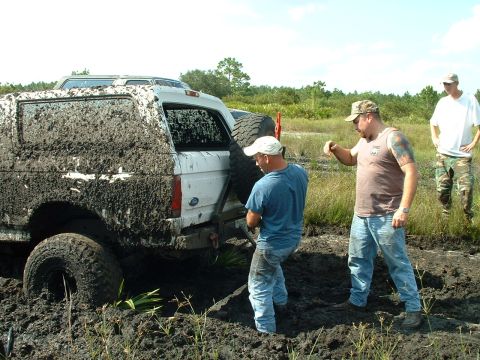 1995 Ford Bronco - A white 1995 Ford Bronco is deeply stuck in mud, with several people gathered around attempting to help.
