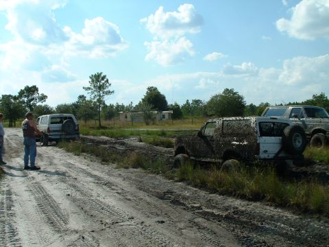 1995 Ford Bronco - Two SUVs are stuck in the mud, with people standing nearby observing the situation.