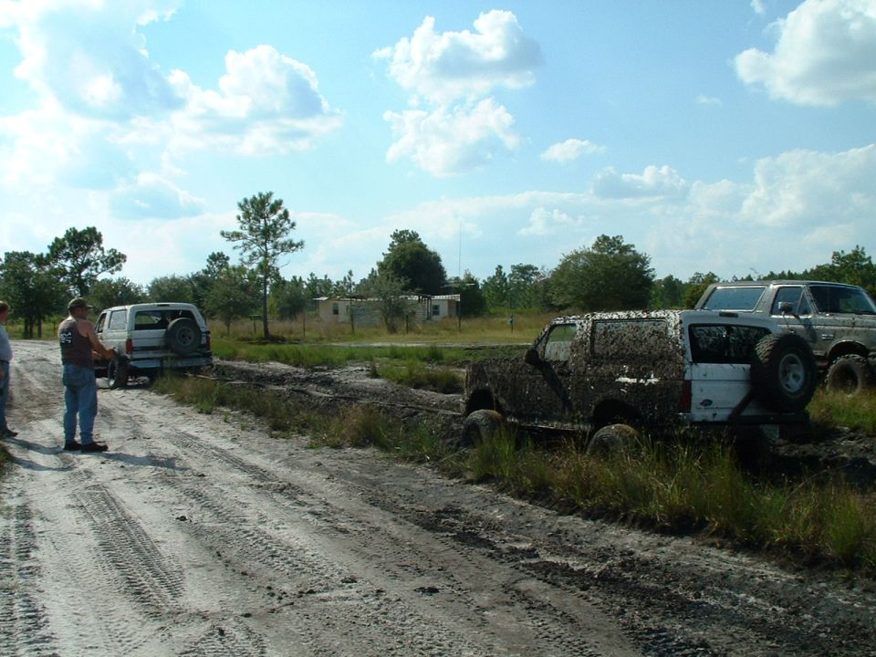 Several SUVs are stuck in thick mud on a dirt track. One is heavily covered in mud, while others are partially submerged
