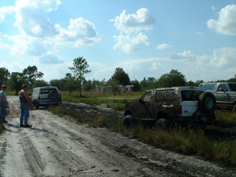 1995 Ford Bronco - Several vehicles are stuck in the mud on a dirt track under a cloudy sky.