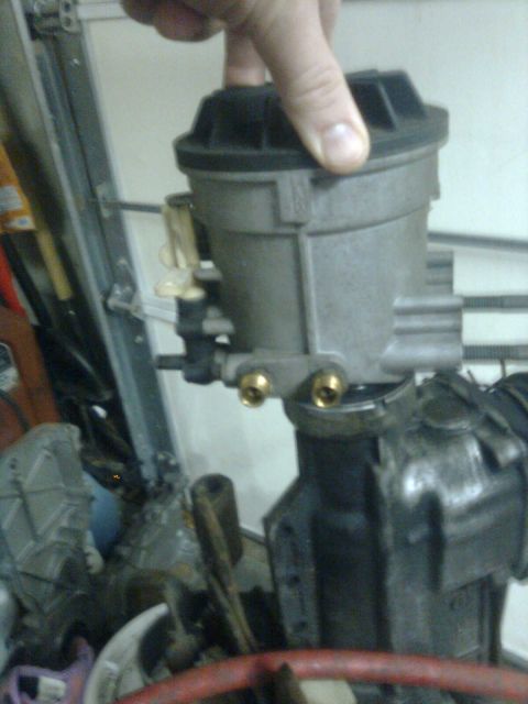 1984 Ford Bronco - A hand holds a gray and black supercharger housing with brass fittings.
