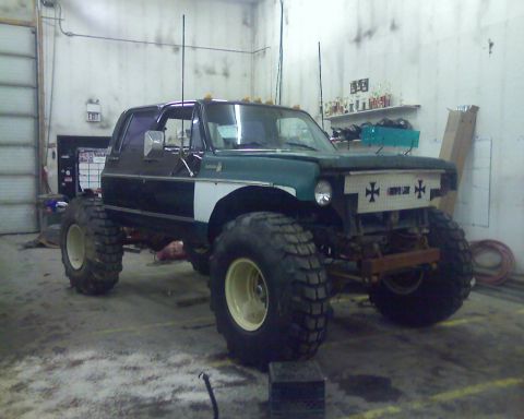 1978 Chevrolet C/K Pickup - Modified 1978 Chevrolet C/K Pickup truck with large off-road tires and custom grille in a garage.