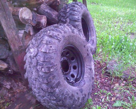 1978 Chevrolet C/K Pickup - Two large off-road tires with aggressive tread patterns are shown leaning against a pile of logs.