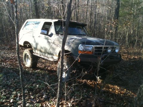 1995 Ford Bronco - This 1995 Ford Bronco is navigating a muddy, wooded trail with its tires partially submerged in the terrain.