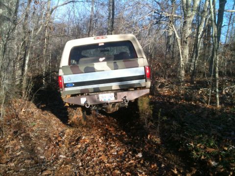 1995 Ford Bronco - This 1995 Ford Bronco is captured from the rear as it navigates a wooded, off-road trail covered in fallen leaves.