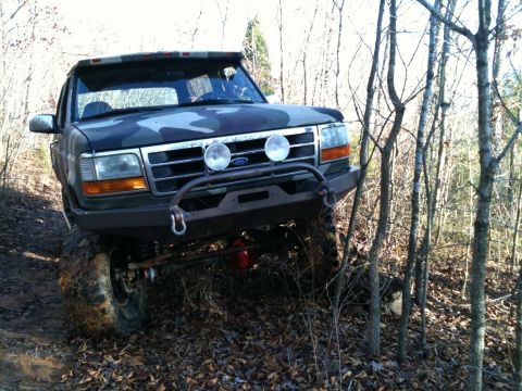 1995 Ford Bronco - A camouflaged Ford Bronco navigates a wooded trail, its off-road modifications.