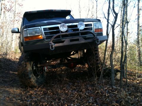 1995 Ford Bronco - This 1995 Ford Bronco is equipped with a custom bumper and off-road tires, navigating a wooded trail.