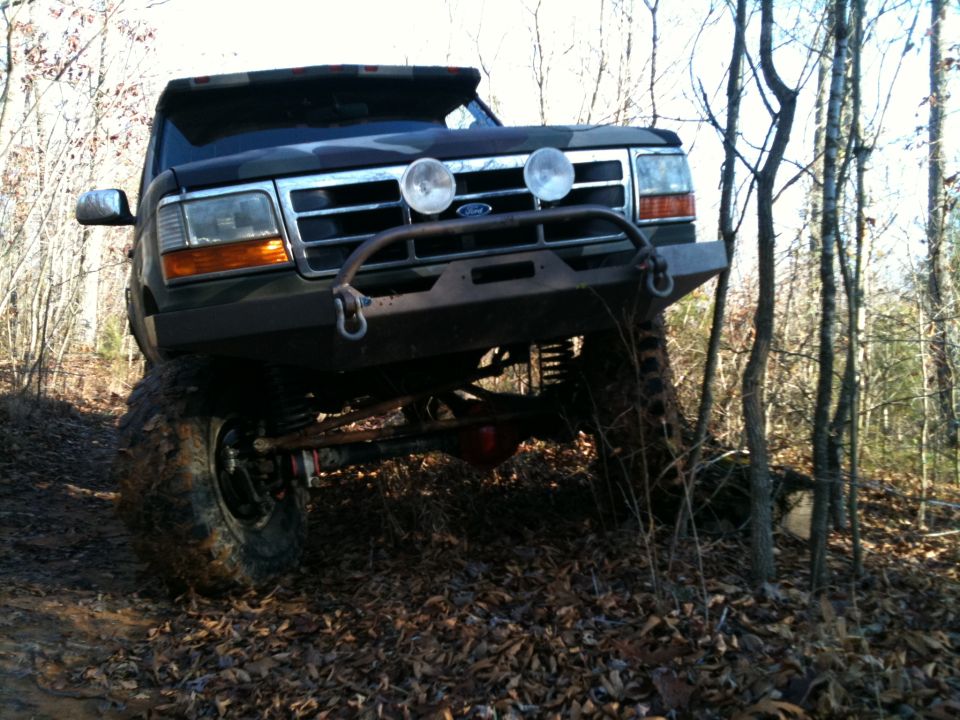 1995 Ford Bronco front end with custom bumper and off-road tires on wooded trail