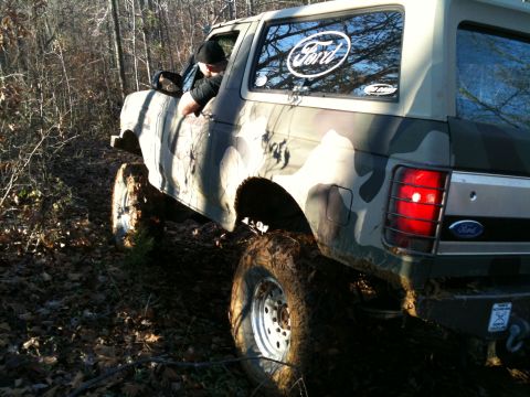 1995 Ford Bronco - A Ford Bronco navigates a muddy, wooded trail with its tires covered in dirt.