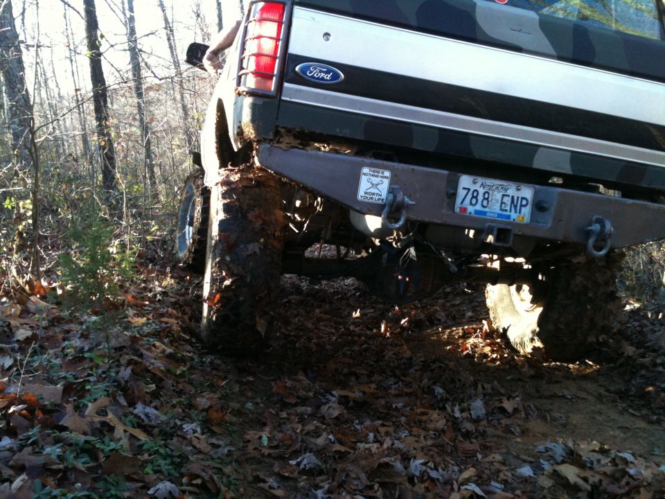 Mud-covered 1992 Ford Bronco rear end with large tires on a wooded trail