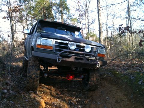1995 Ford Bronco - This lifted Ford truck is navigating a muddy, wooded path.