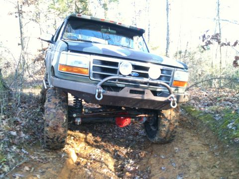 1995 Ford Bronco - This lifted Ford Bronco is navigating a challenging muddy terrain with its camouflage paint job.