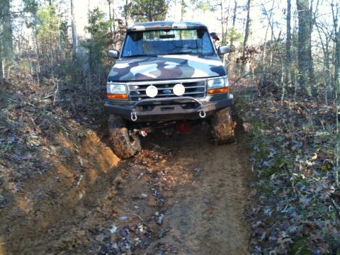 1995 Ford Bronco - This 1995 Ford Bronco is navigating a challenging muddy path in a wooded area.