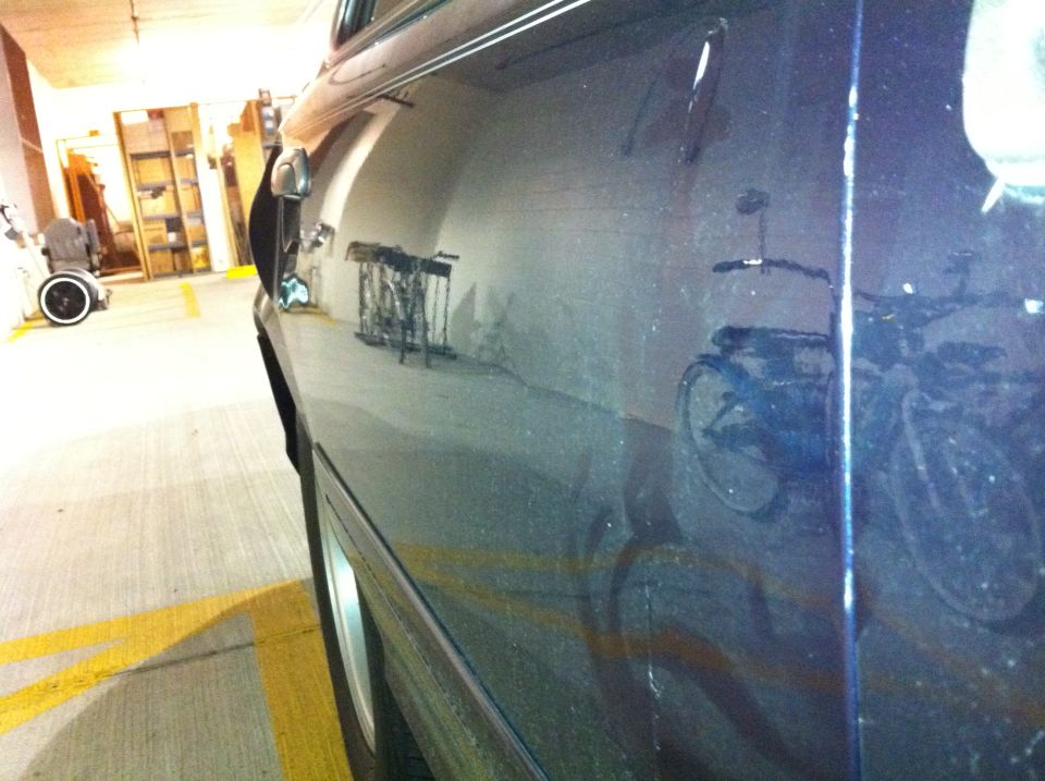 Reflection of bicycles on the side of a dark-colored car parked indoors