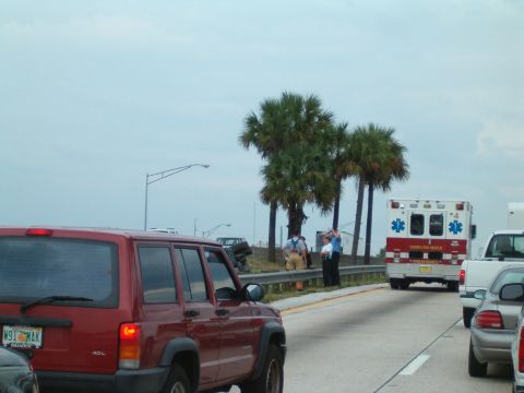 1991 Ford Bronco - Red SUV and ambulance on a highway with palm trees under a cloudy sky.