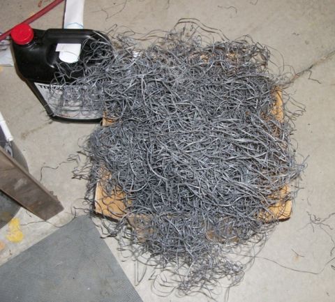1996 Ford Bronco - A large pile of metal shavings sits on a wooden pallet next to a black fluid container with a red cap.