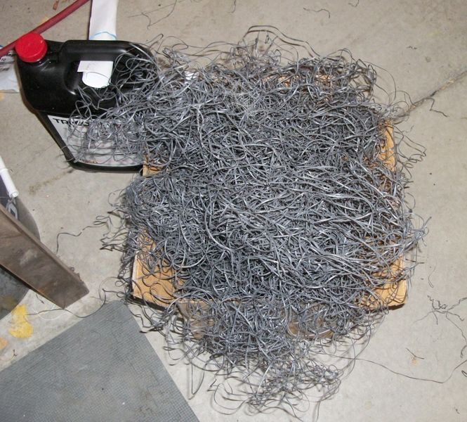 Pile of metal shavings next to a black fluid container with a red cap
