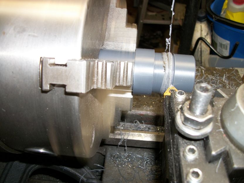 Lathe chuck gripping a gray pipe being machined with metal shavings on the bed