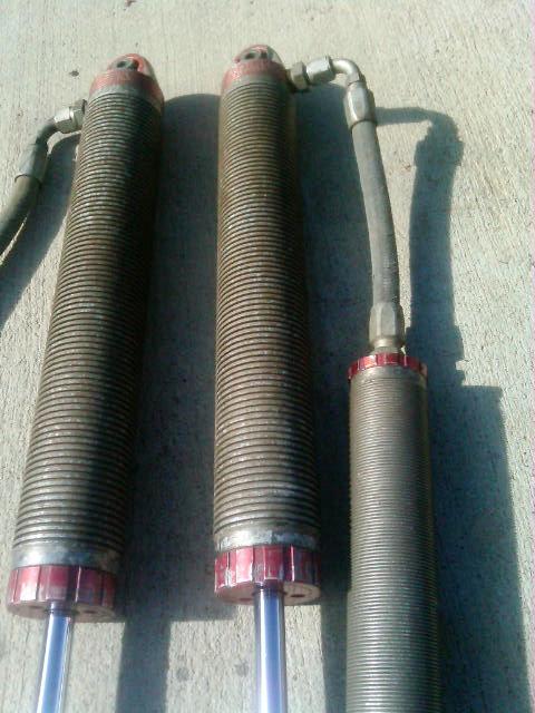 1986 Ford Bronco - Three shock absorbers with red accents are laid out on a concrete surface.
