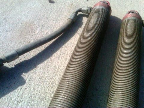 1986 Ford Bronco - Two shock absorbers with hydraulic lines are shown resting on a concrete surface.