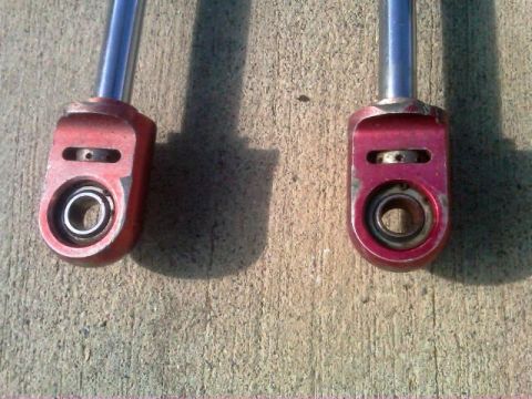 1986 Ford Bronco - Close-up of two red shock absorber ends, each with a bearing and metal shaft.
