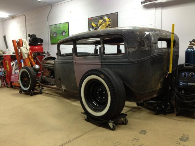 Hot rod sedan with black body and maroon doors, on dollies in a garage. Whitewall tires visible