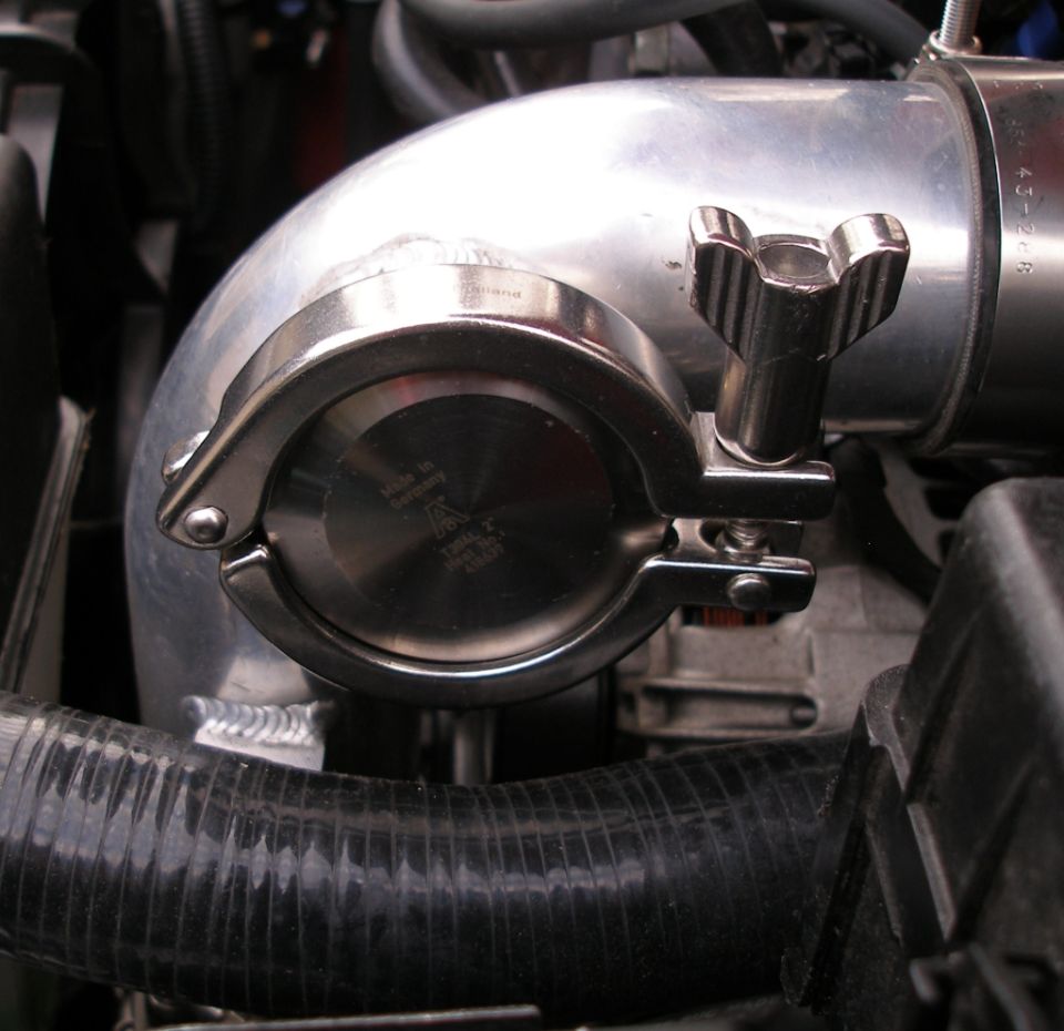 Close-up of a metal pipe clamp with 'Made in Germany' text, attached to a silver pipe in an engine bay