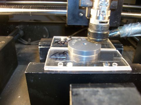 1996 Ford Bronco - A metal disc with engraved text is positioned on a clear plastic plate under a machine's tool.