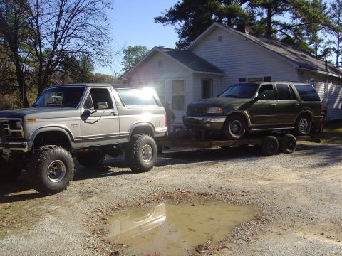 1986 Ford Bronco - 1986 Ford Bronco tows a Ford Expedition on a trailer in front of a house.