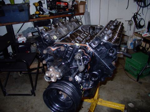 1983 Chrysler Fifth Avenue - A black engine sits on a stand in a cluttered garage, ready for rebuild.
