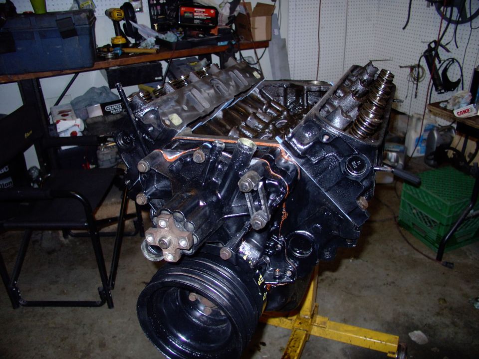 Black V8 short block on yellow engine stand, intake manifold off, valve springs exposed, in garage
