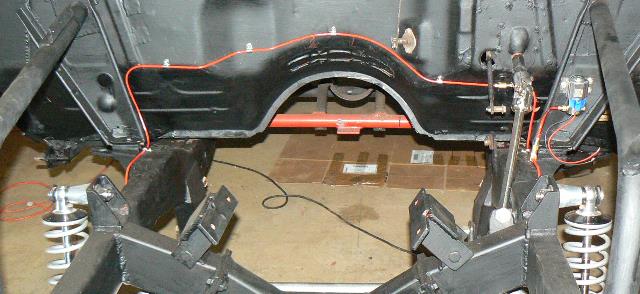 Underbody view of car chassis with suspension and drivetrain components, red wiring visible